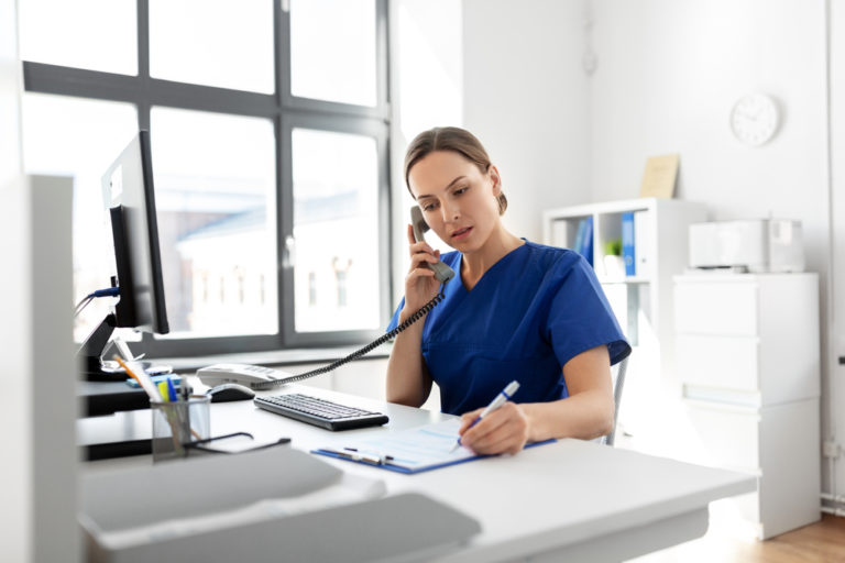 nurse sitting at a desk in front of a computer and answering the phone