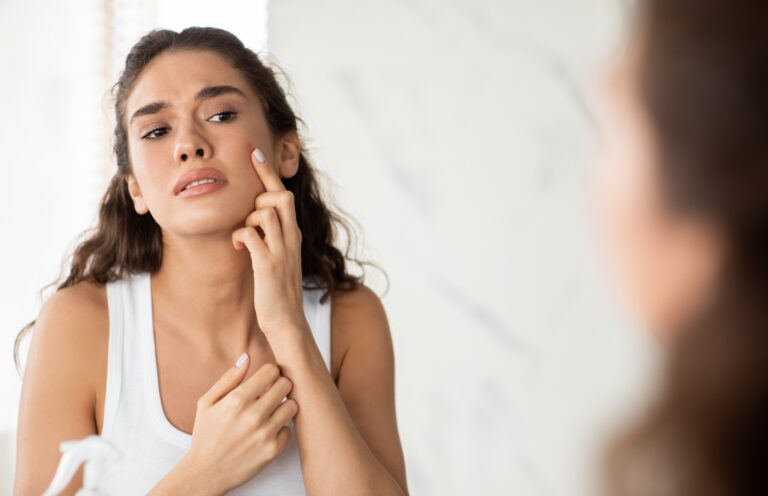 woman looking in mirror and noticing acne and pimple on face